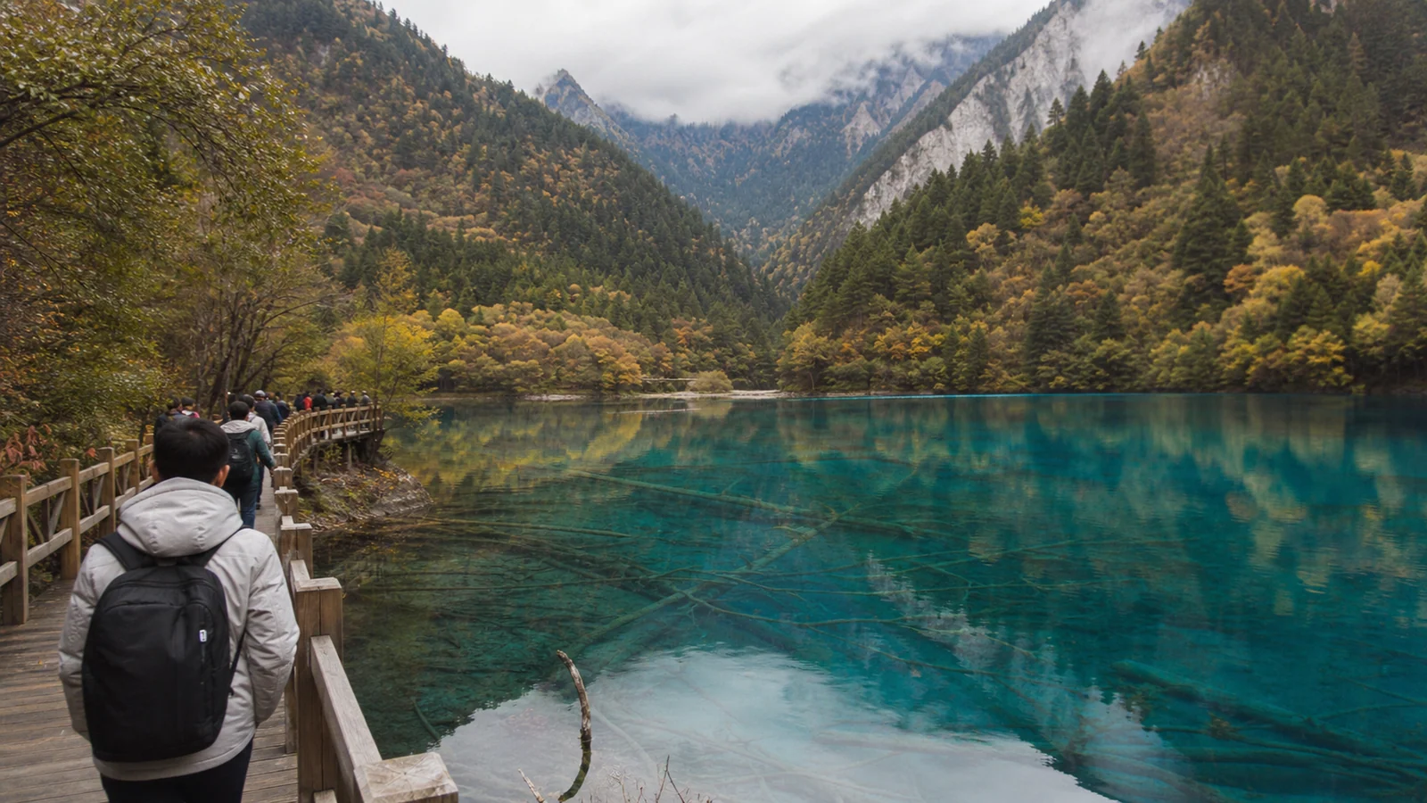 Travelers walking beside a clear blue lake in Jiuzhaigou