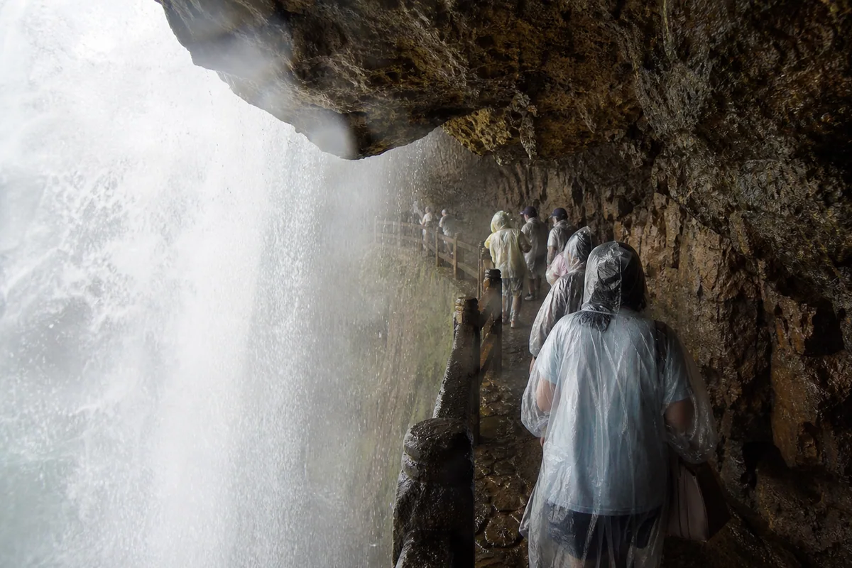 Visitors in rain covers walking behind Huangguoshu Waterfall in the Water Curtain Cave