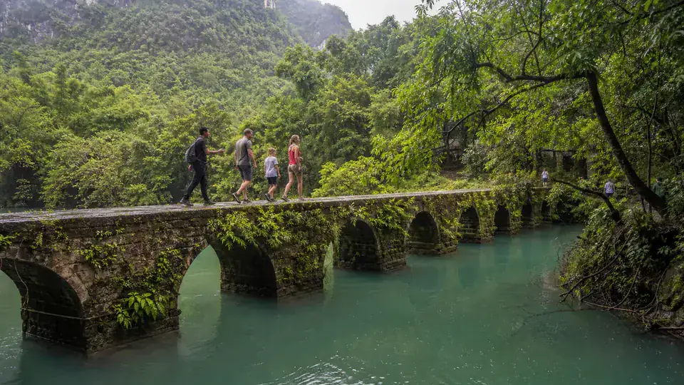 Family crossing the old seven arch bridge at Xiaoqikong in Libo