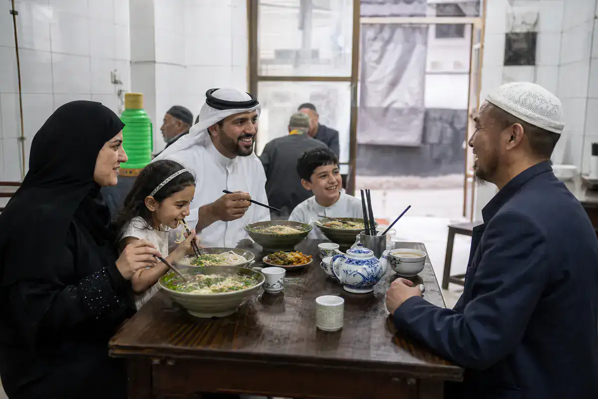 Gulf Muslim family sharing a halal noodle meal with a Chinese Muslim host in Xi’an