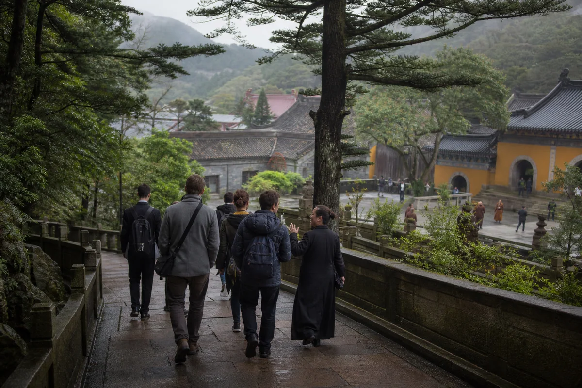 International visitors walking quietly with a guide toward a Putuoshan temple