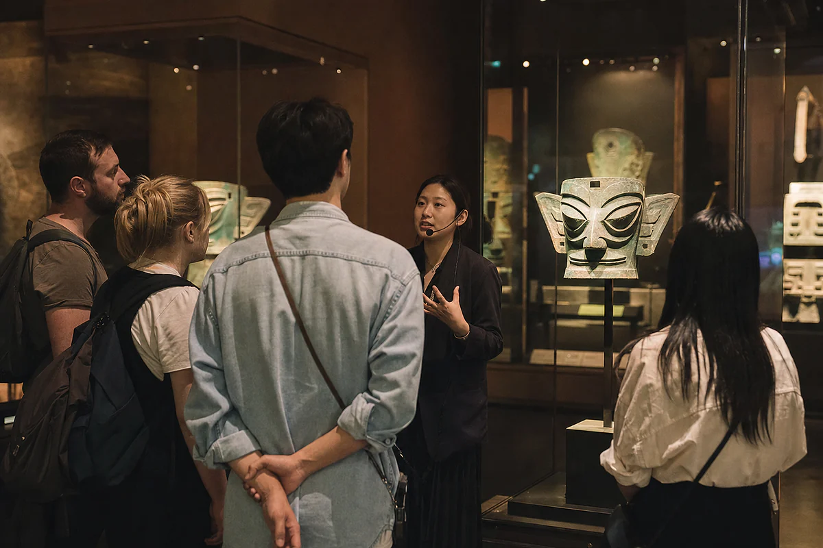 International visitors listening to a guide beside an ancient Shu bronze mask display