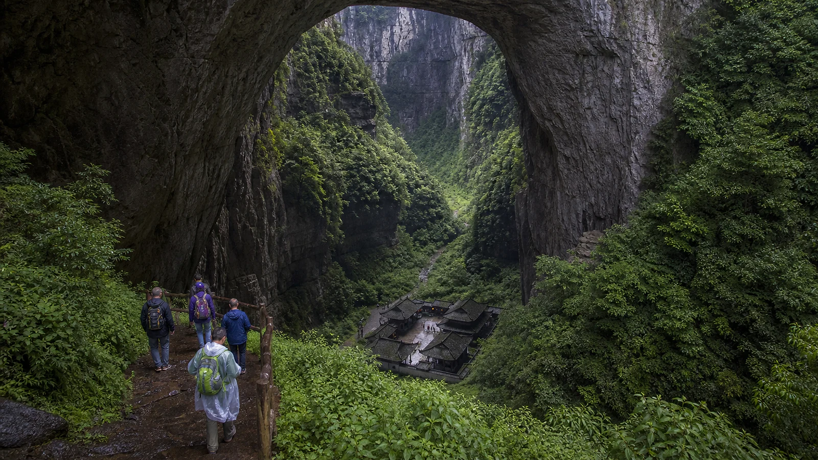 Visitors descending beneath a giant limestone arch toward Tianfu post station at Wulong Karst