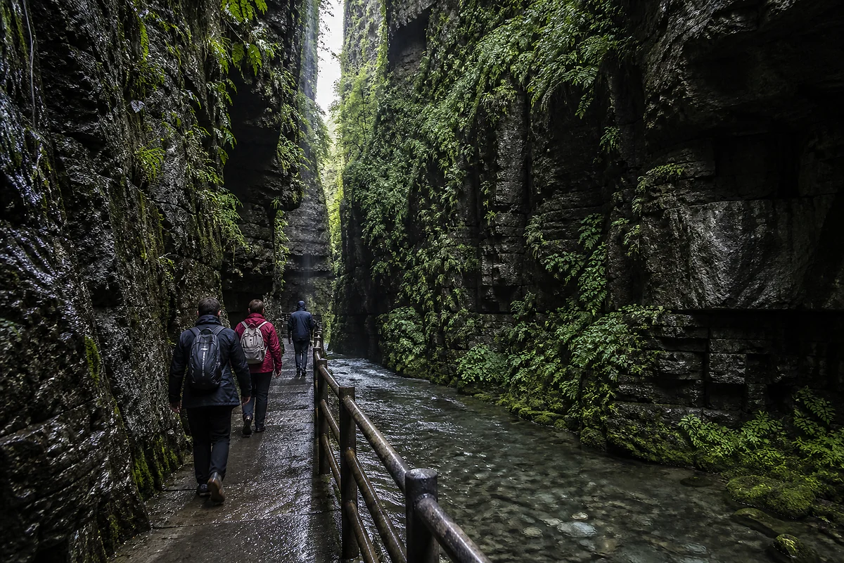 Travelers walking beside clear water between wet limestone walls in Longshuixia Fissure Gorge