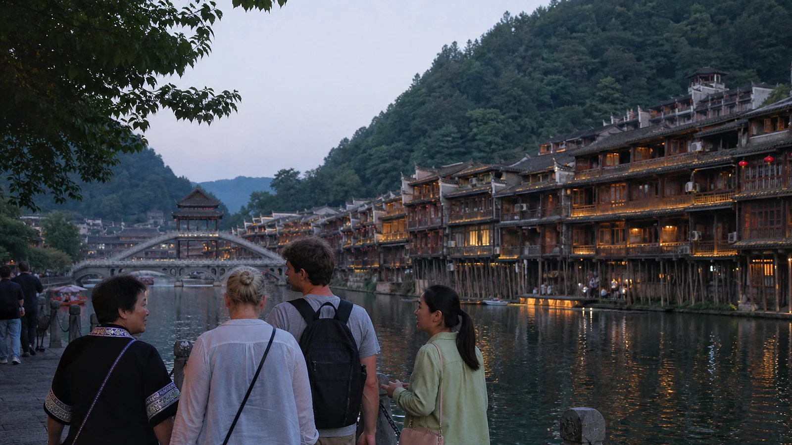 Visitors with a local guide beside the Tuojiang River and stilt houses of Fenghuang at blue hour
