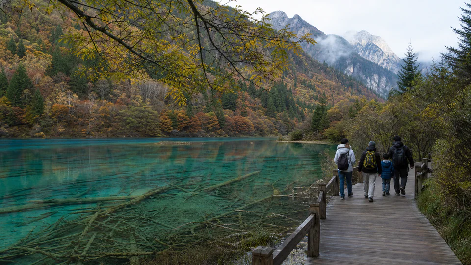 A family walking beside a turquoise lake in Jiuzhaigou with a private guide