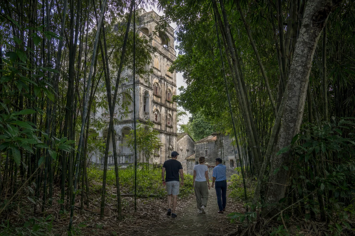 Travelers and a local guide walking through bamboo toward a weathered diaolou in Majianglong village