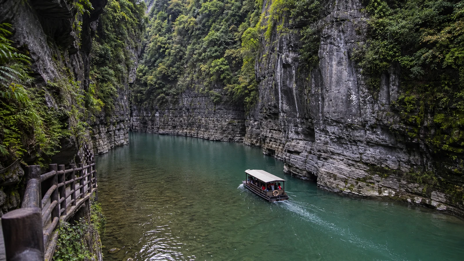 Sightseeing boat moving through the clear blue green water and layered limestone walls of Pingshan Canyon