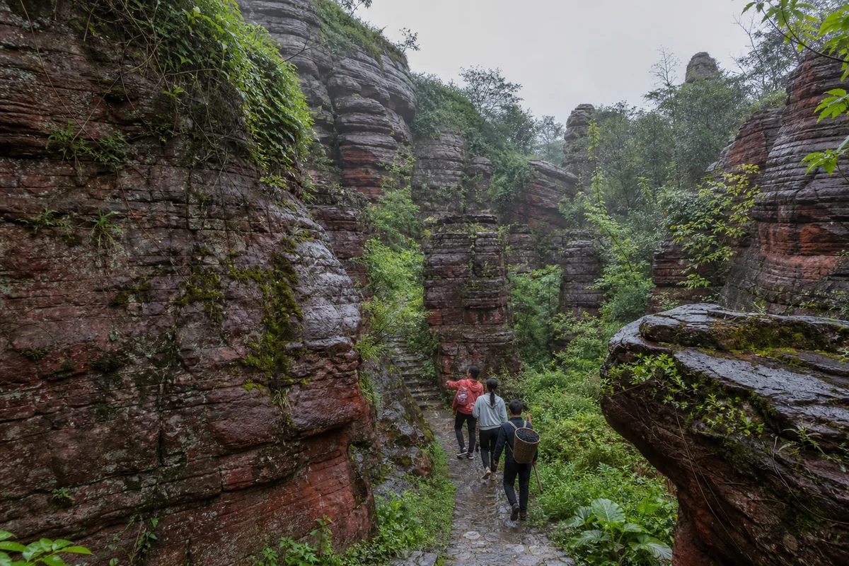 Travelers following a wet path between red rock formations in Xiangxi Red Stone Forest